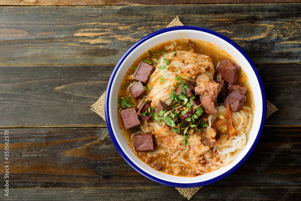 Northern Thai food (Kanom Jeen Nam Ngeaw), Rice noodles spicy soup with pork and pork blood in bowl on wooden background Northern Thai food (Kanom Jeen Nam Ngeaw), Rice noodles spicy soup with pork and pork blood in bowl on wooden background