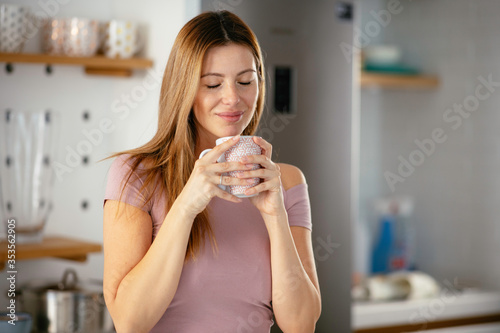  Beautiful woman drinking coffee in the kitchen. Young woman enjoy at home.