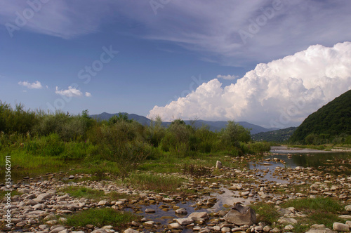 landscape with mountain river and cumulus clouds on a summer day before rain