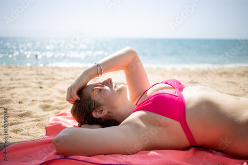 young caucasian girl in pink glasses lies on a sandy beach in a pink bikini swimsuit on a background of sea waves