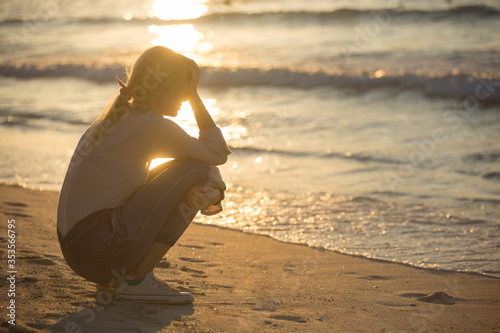 Foto Sad depressed young woman sitting alone with hand on face at the beach near the water during sunset