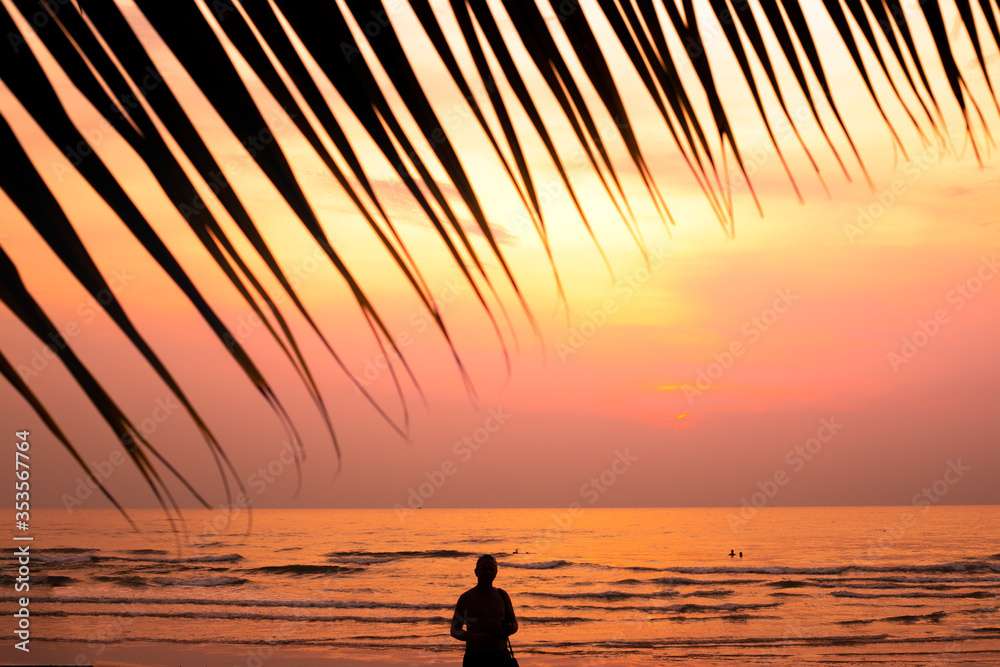 bright orange sunset on the sea coast in the tropics, a silhouette of a tourist and palm leaves
