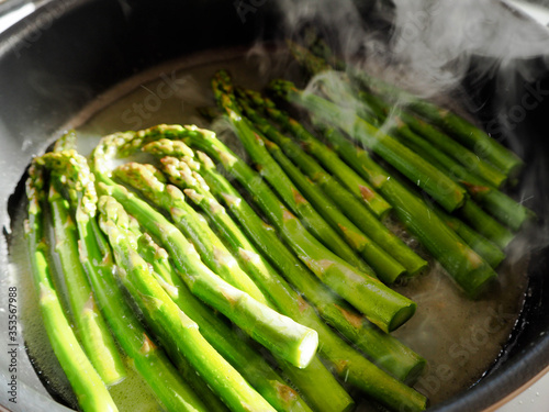 green asparagus stalks are fried in a large pan with a evaporating liquid . caramelization asparagus with sugar, salt, water and butter . couples