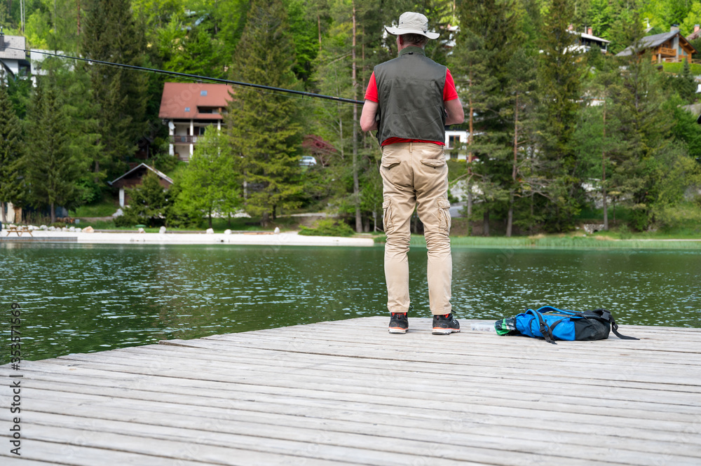 Fisherman standing on wodden pier catching fish.