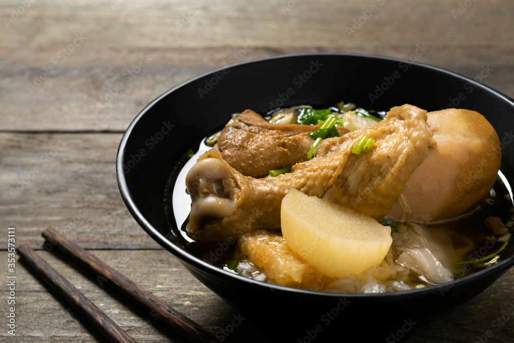Rice noodle with chicken leg in black bowl on wooden table.