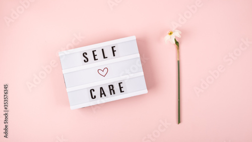 Self-care word on lightbox and flower narcissus on pink background flat lay. Take care of yourself photo