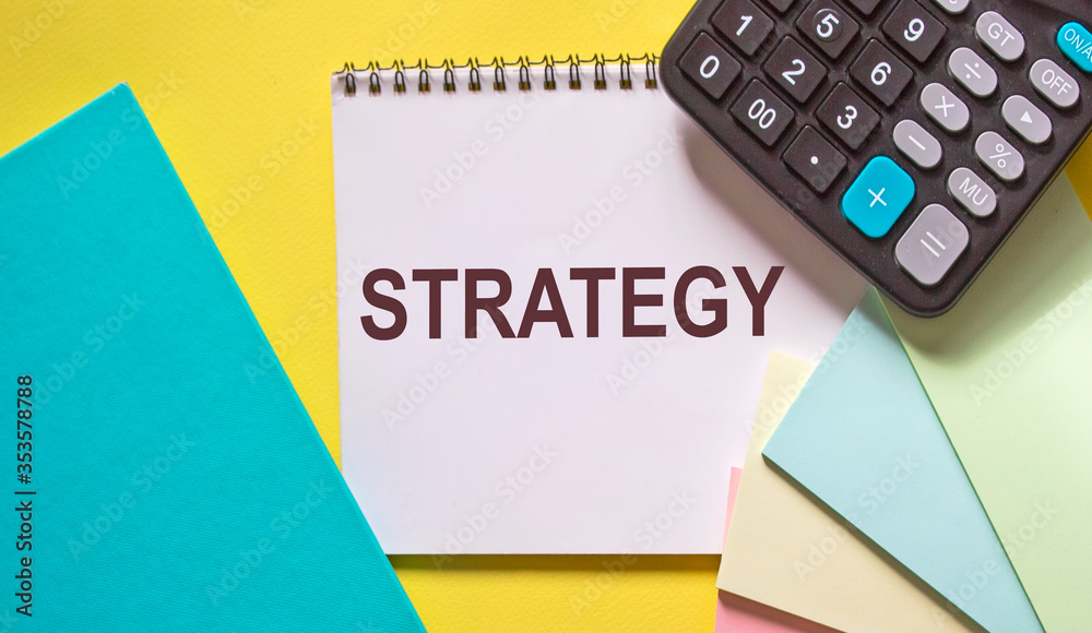 The text strategy in a notebook on a yellow background, next to multi-colored stickers, a turquoise notebook and a calculator. The text strategy in a notebook on a yellow background, next to multi-colored stickers, a turquoise notebook and a calculator.