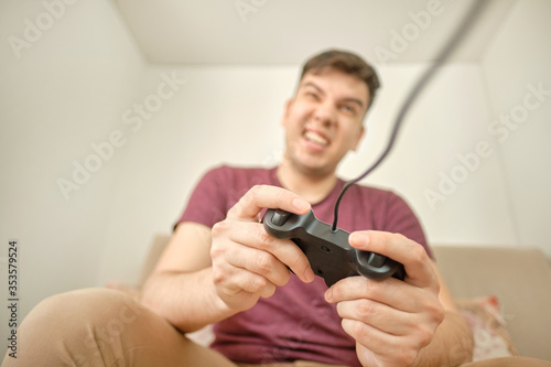 Excited young handsome man playing video game while sitting on the couch at home. Happy man playing video games on weekend.