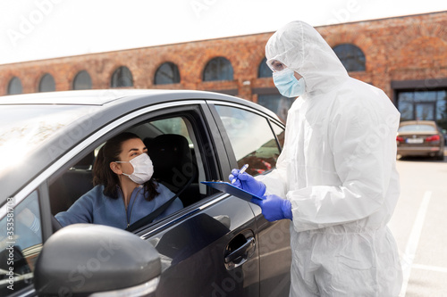 medicine, quarantine and pandemic concept - doctor or healthcare worker in protective gear, medical mask, gloves and goggles with clipboard and woman waiting for coronavirus test in her car © Syda Productions