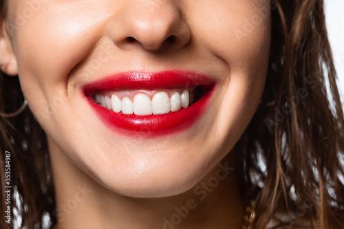 Close up of beautiful female smile with white teeth isolated on white studio background. Caucasian brunette model with bright red lipstick  wet hair and shiny skin. Beauty  fashion  emotions concept.