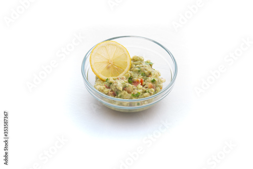 Homemade Guacamole in a glass bowl. Healthy breakfast with lemon. Isolated on white.