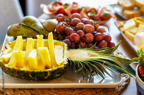 Plate of fresh sliced fruits - juicy pineapple, grapes, pears and other snacks.