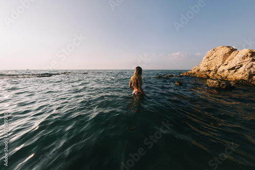 Girl with long hair swims in the sea, splashes water on a background of a sunset sky