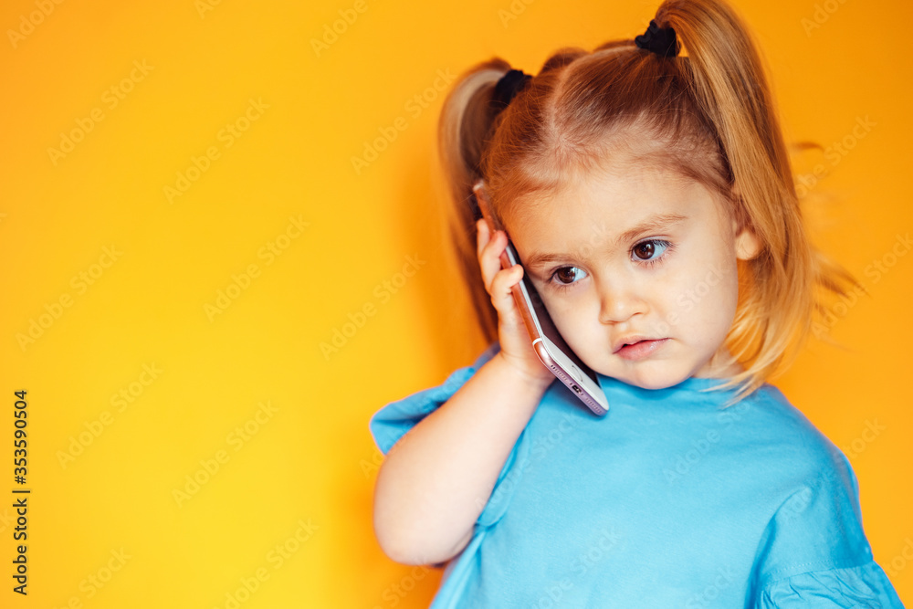 cute girl with ponytails uses a smartphone, smiling toddler, on an orange background, close-up, telephone conversation, telephone connection cute girl with ponytails uses a smartphone, smiling toddler, on an orange background, close-up, telephone conversation, telephone connection