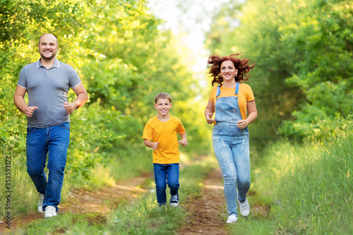 Cheerful parents with son in casual wear smiling run on nature on a summer evening