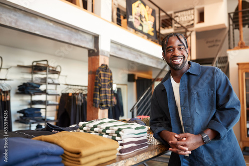 Фотография Portrait Of Smiling Male Owner Of Fashion Store Standing In Front Of Clothing Di