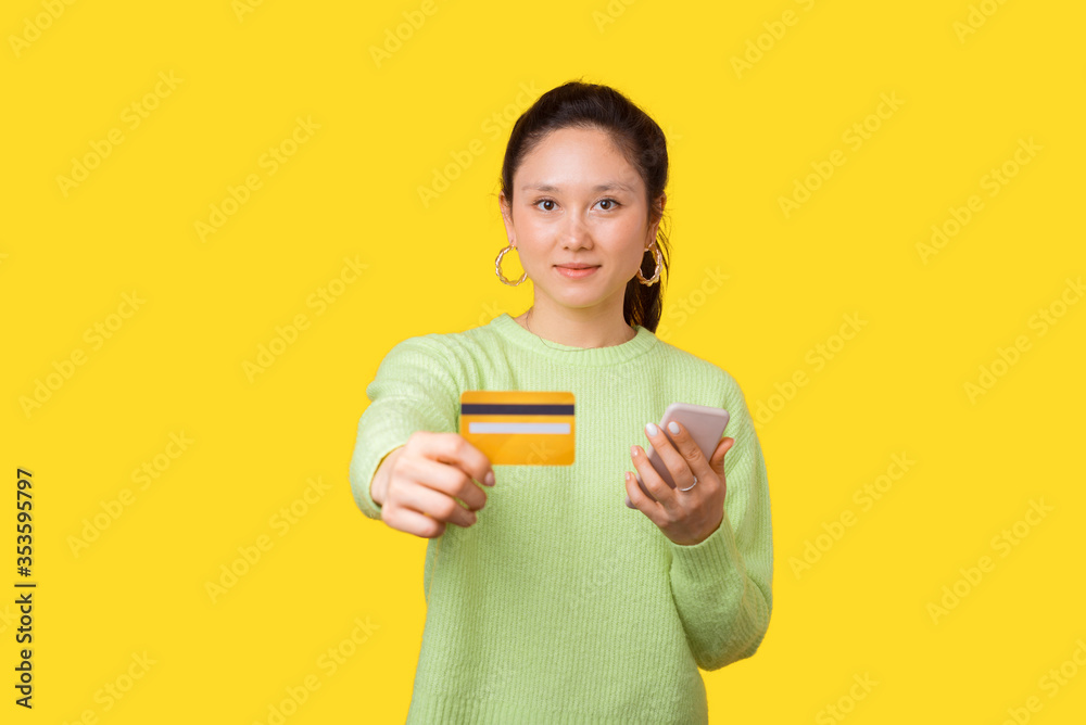 Beautiful simple girl is showing you a credit or debit card and holding phone to use mobile banking Beautiful simple girl is showing you a credit or debit card and holding phone to use mobile banking
