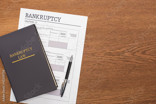 top view of bankruptcy paper, law book and pen on wooden background photo