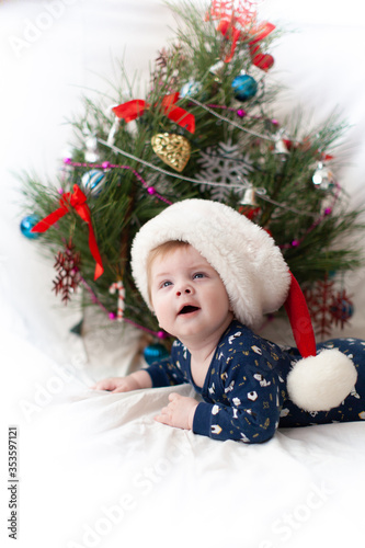 infant in santa hat near christmas tree new year