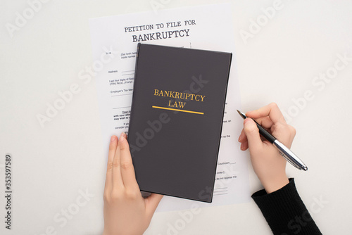 cropped view of woman with bankruptcy paper, law book and pen on white background photo
