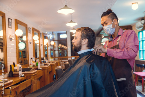Beard styling. Barber shaping beard of handsome man using a trimmer. Skilled barber trimming beard to his client