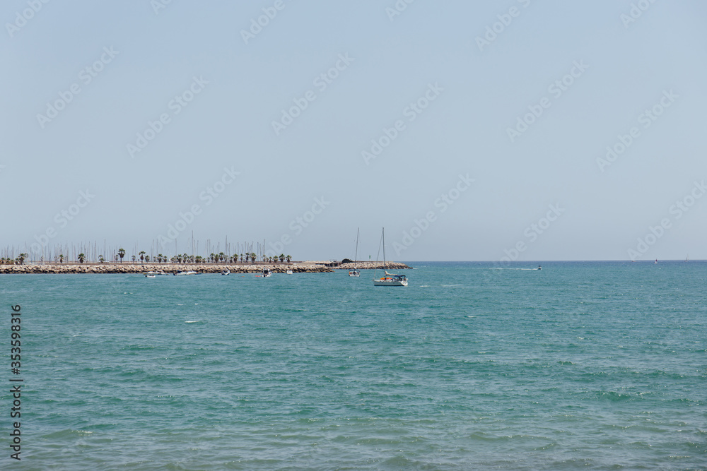 Yachts in sea near pier with blue sky at background in Catalonia, Spain
