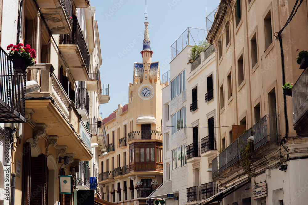 Urban street with clock on chapel and blue sky at background in Catalonia, Spain
