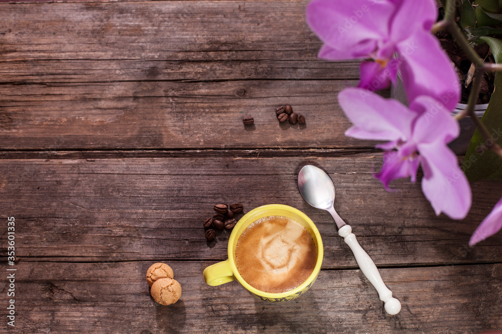 Cup of coffee on wooden table with coffee beans and amaretti, orchid in background Cup of coffee on wooden table with coffee beans and amaretti, orchid in background