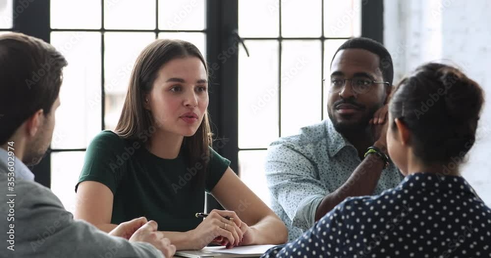 Young female team leader sitting at table with mixed race colleagues, discussing working issues at negotiations meeting. Skilled millennial diverse employees developing startup marketing strategy.