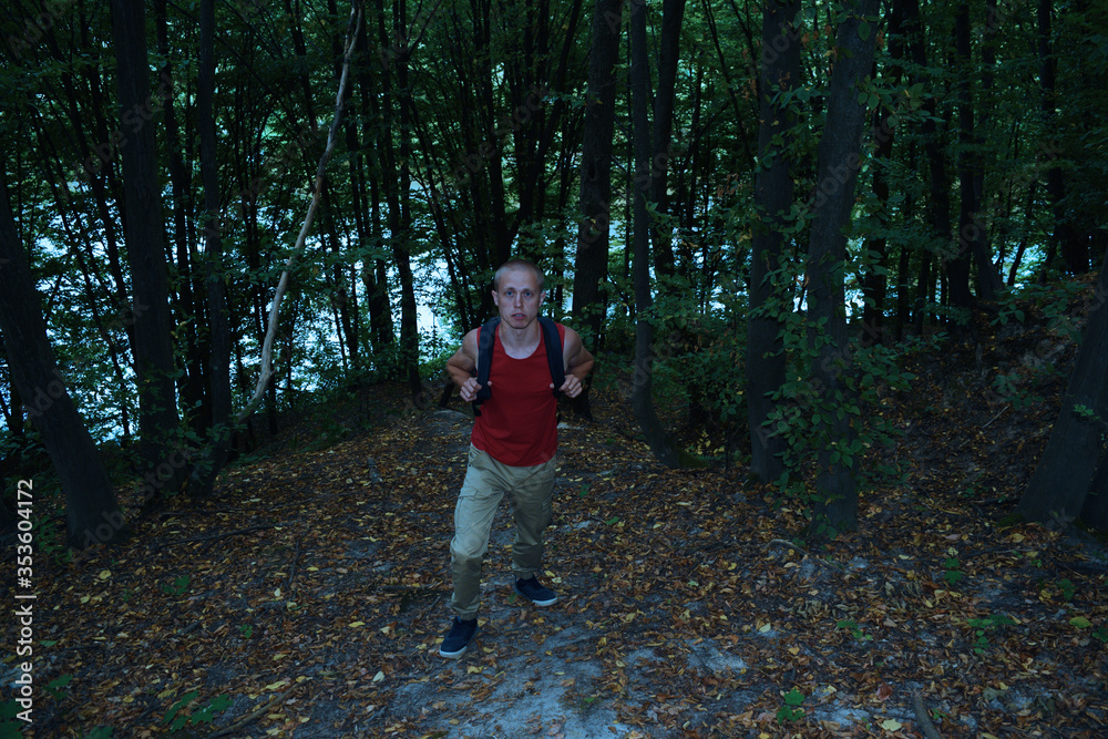 Top view on a young tourist man with a backpack in a dark forest. Outdoor travel