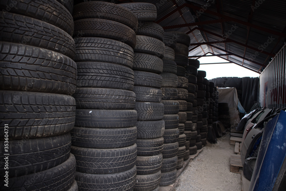A lot of used and worn tires from cars one on top of each other. Also, some automobile doors. Inside a warehouse. At a vehicle graveyard. For recycle or re-sale. Kozani. Greece. A lot of used and worn tires from cars one on top of each other. Also, some automobile doors. Inside a warehouse. At a vehicle graveyard. For recycle or re-sale. Kozani. Greece.