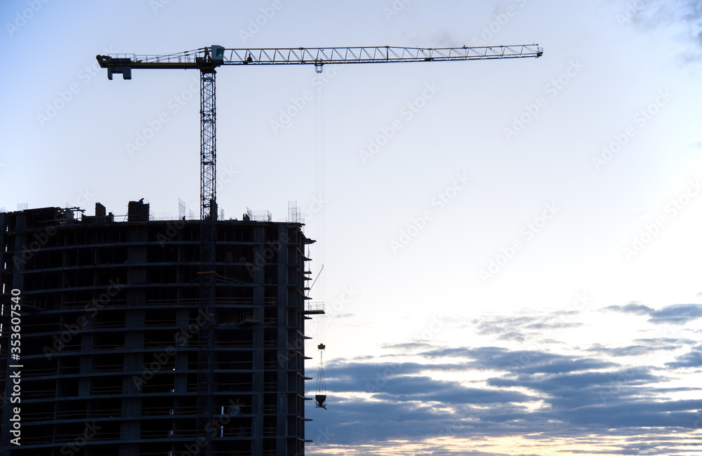 Silhouettes of tower cranes in action on sunset. Preparing to pour a bucket of concrete into formwork. Construction a residential building. Small sharpness, possible granularity Silhouettes of tower cranes in action on sunset. Preparing to pour a bucket of concrete into formwork. Construction a residential building. Small sharpness, possible granularity