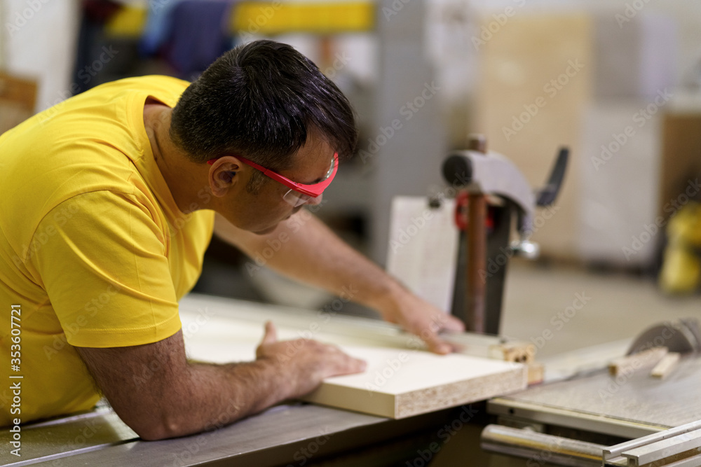Carpenter cutting a piece of wood for furniture in his woodwork workshop, using a circular saw, and wearing safety goggles. Carpenter cutting a piece of wood for furniture in his woodwork workshop, using a circular saw, and wearing safety goggles.