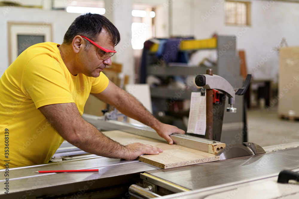 Carpenter cutting a piece of wood for furniture in his woodwork workshop, using a circular saw, and wearing safety goggles. Carpenter cutting a piece of wood for furniture in his woodwork workshop, using a circular saw, and wearing safety goggles.