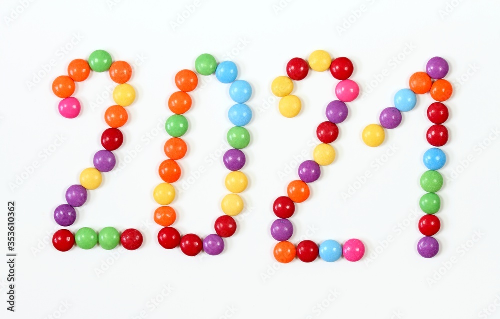 2021, colorful smarties on white background. Chocolate candies in shape of buttons, top view.