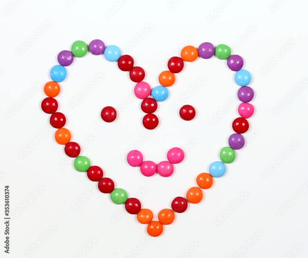 Smiling heart made from colored smarties. Chocolate candies in a shape of heart with smile on face, white background, Smiling heart made from colored smarties. Chocolate candies in a shape of heart with smile on face, white background,