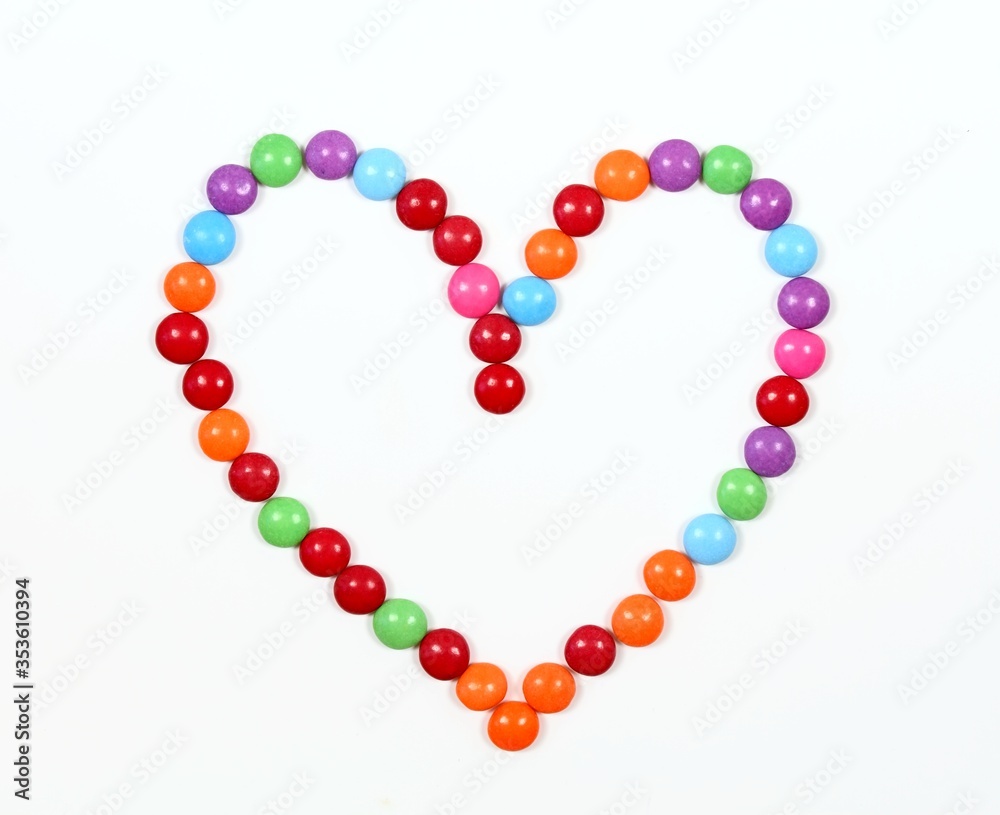 Sweet heart made from colored smarties. Chocolate candies in a shape of heart on white background, top view. Sweet heart made from colored smarties. Chocolate candies in a shape of heart on white background, top view.