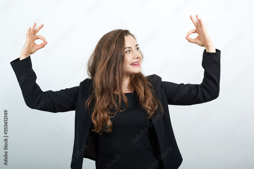 Young Attractive Woman Brunette In In Black T-Shirt And Sweater On White Background, Happy Female Smiles Raised Hands Up, Makes, Ok Sign With Her Fingers. Concept Of Happy People, Everything Is Fine Young Attractive Woman Brunette In In Black T-Shirt And Sweater On White Background, Happy Female Smiles Raised Hands Up, Makes, Ok Sign With Her Fingers. Concept Of Happy People, Everything Is Fine