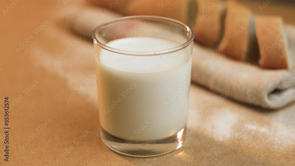 Drops of milk splashes in a full glass on a light background. Milk Day in the world. Vegetable drink against the background of baguette