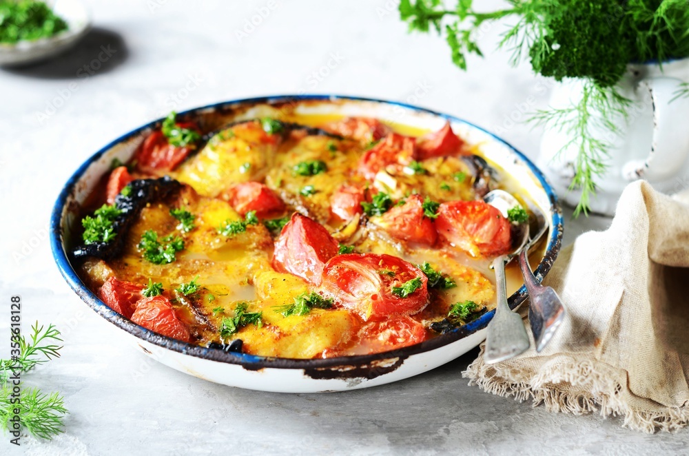 Baked fish (shark) with tomatoes and spices in a baking dish on a gray background, still life