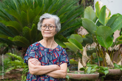 Portrait of an elderly woman arms crossed and smiling while standing in garden