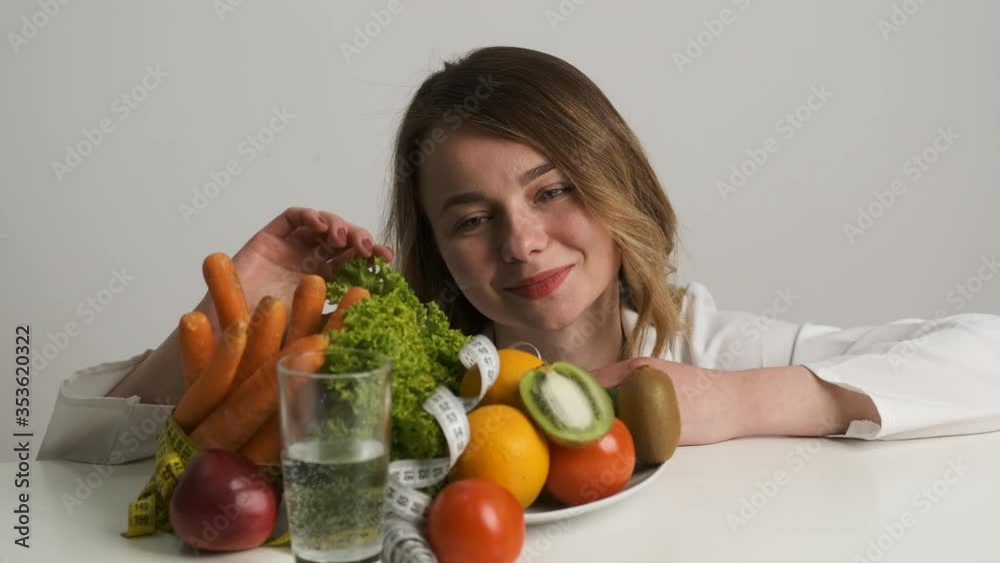 Diet and health. A female doctor of Caucasian appearance licks at the table and admires fruits and vegetables Diet and health. A female doctor of Caucasian appearance licks at the table and admires fruits and vegetables