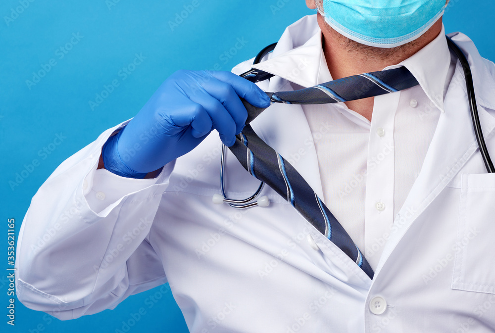 adult male doctor in a white coat tears off his tie, blue background adult male doctor in a white coat tears off his tie, blue background