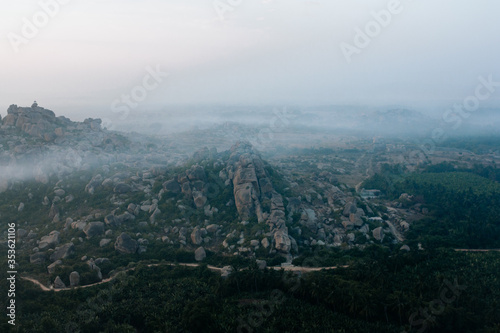 Panoramic view of morning fog enveloping stone hills and banana groves in Hampi during sunrise