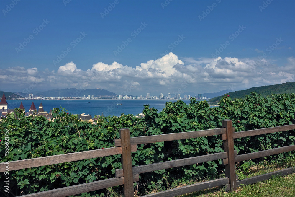 Beautiful vietnamese landscape. Park on the island, behind the fence grow green shrubs. Ships at sea. In the distance are the silhouettes of the city buildings, the outlines of the mountains. Clouds. Beautiful vietnamese landscape. Park on the island, behind the fence grow green shrubs. Ships at sea. In the distance are the silhouettes of the city buildings, the outlines of the mountains. Clouds.