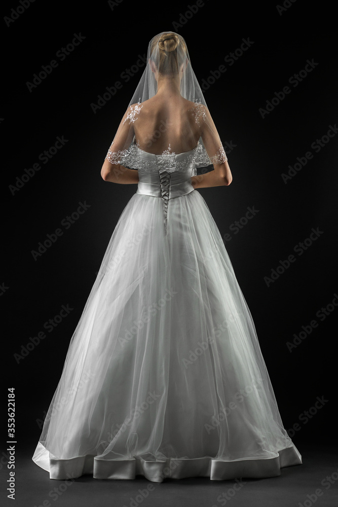 Bride in a beaituful long white wedding dress and lace bridal veil, back view. Black background Bride in a beaituful long white wedding dress and lace bridal veil, back view. Black background