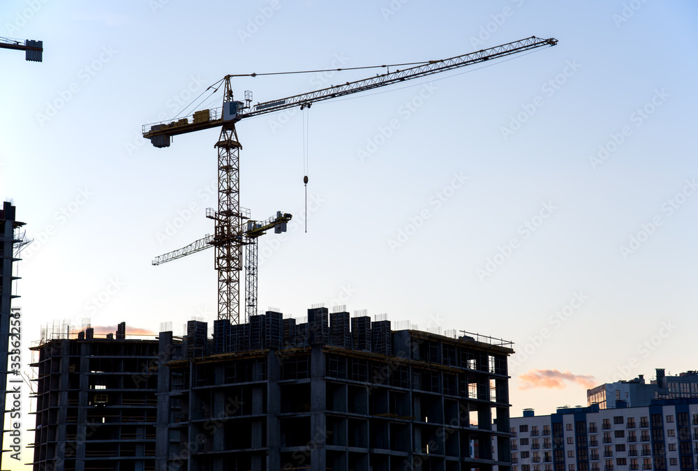 Tower cranes in action during construction residential building on blue sky background. Builder workers during formwork and pouring concrete. Crane lifting a concrete bucket and blocks