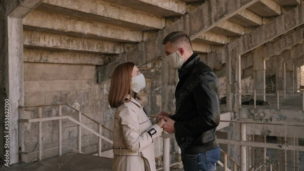 A couple in love with protective medical masks on their faces stand hugging and kissing against the background of an old dilapidated building. New coronavirus (COVID-19). A couple in love with protective medical masks on their faces stand hugging and kissing against the background of an old dilapidated building. New coronavirus (COVID-19).