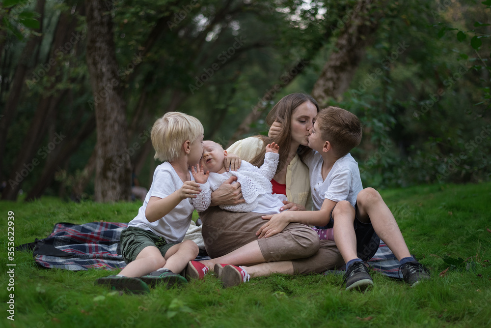 Family picnic at garden outdoors. Mother and three children sitting on picnic blanket in the Park. Mom kisses son