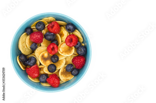 Healthy breakfast of tiny pancake cereal with berries in a blue bowl on a white background. Top view. space for text.